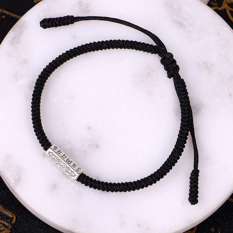 Le bracelet "Mantras" en Fil Rouge de couleur noire sur une plaque de marbre ronde