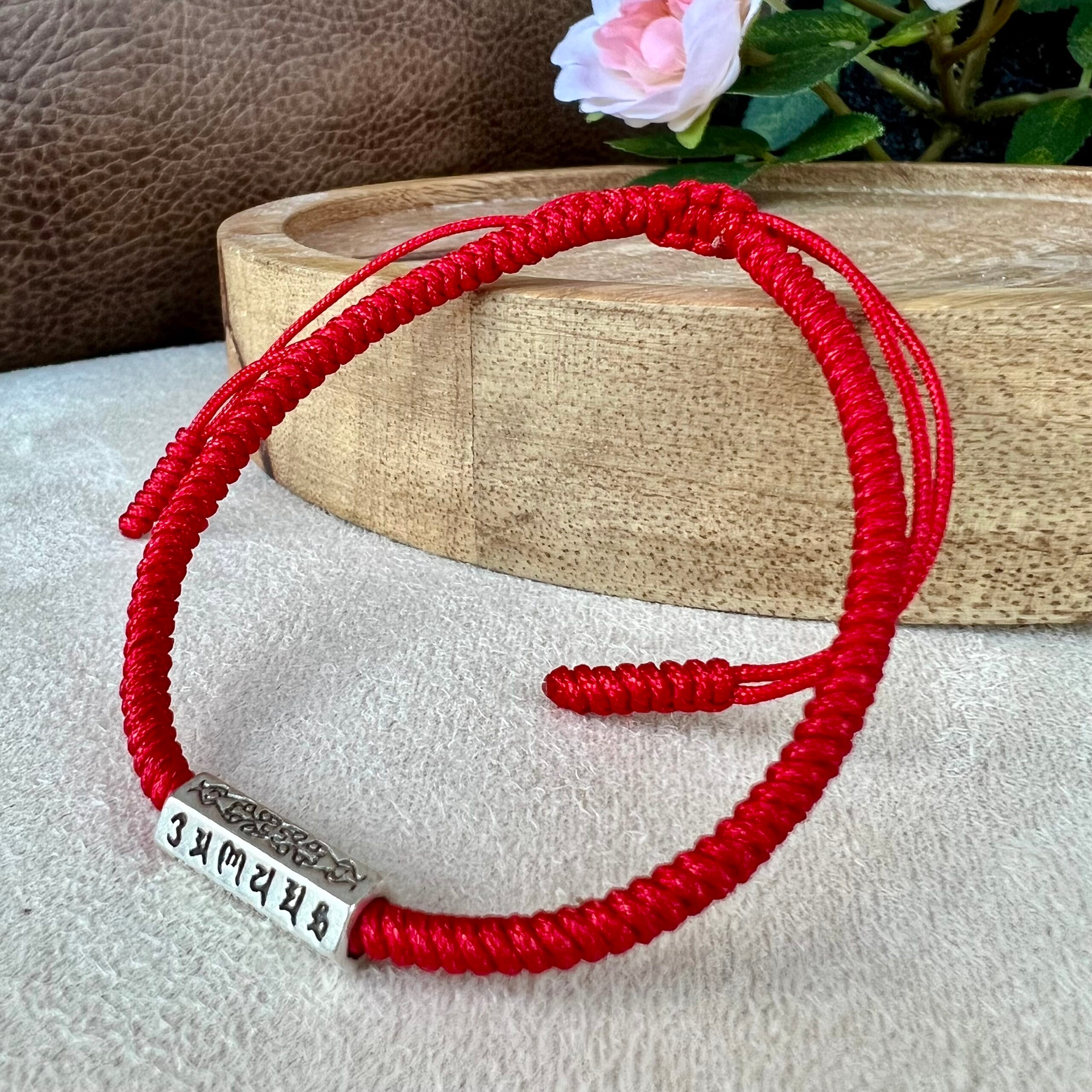 Le bracelet "Mantras" en Fil rouge à côté d'un plateau en bois et d'un plante