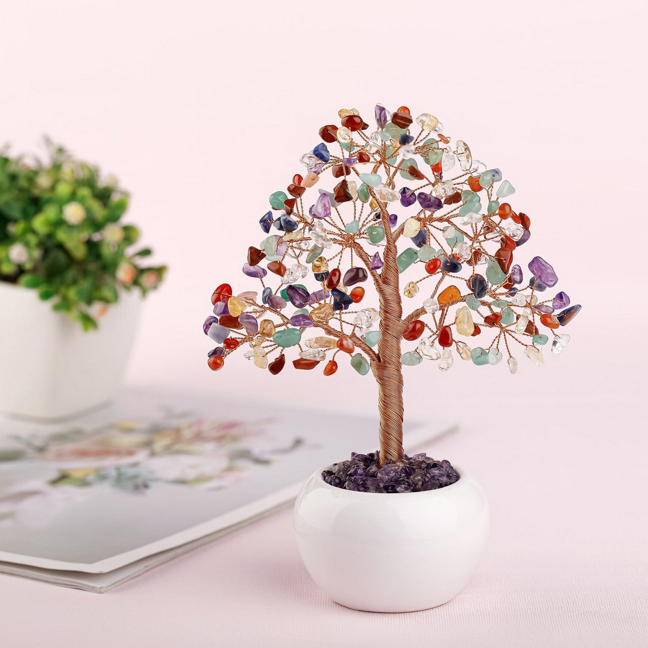 Arbre de vie multicolore en pierres naturelles et fil de cuivre, posé dans un pot blanc, sur un fond rose pâle.