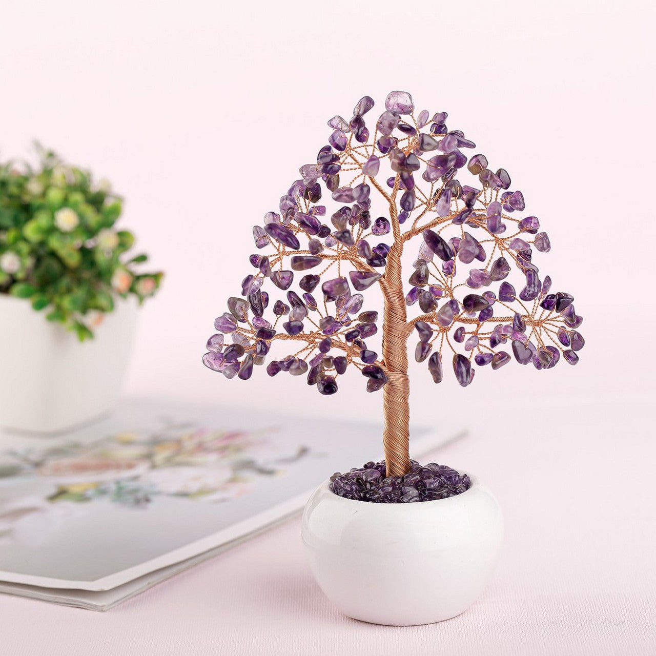Arbre de vie décoratif en améthyste et fil de cuivre, posé dans un pot blanc sur un fond rose pâle. La décoration est ornée de 7 chakras.