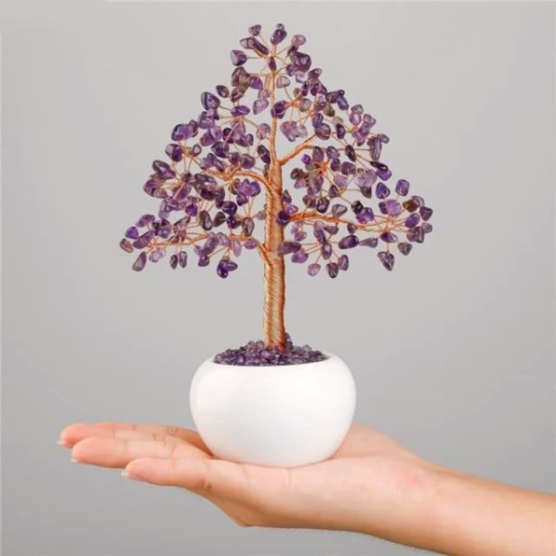 Arbre de vie décoratif avec des pierres d'améthyste violettes et un tronc en fil de cuivre, posé dans un pot blanc tenu dans une main.