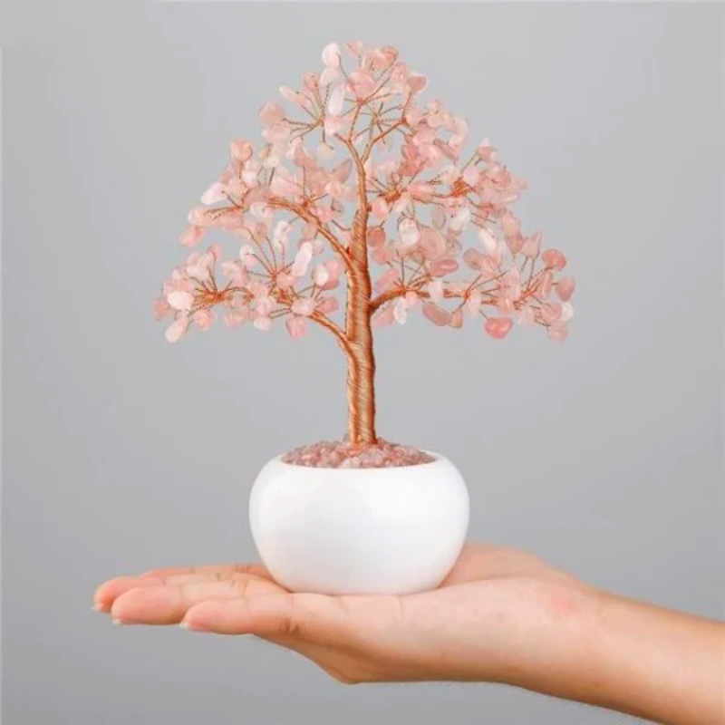 Arbre de vie décoratif en pierres roses et fil de cuivre, posé sur une main dans un pot blanc.