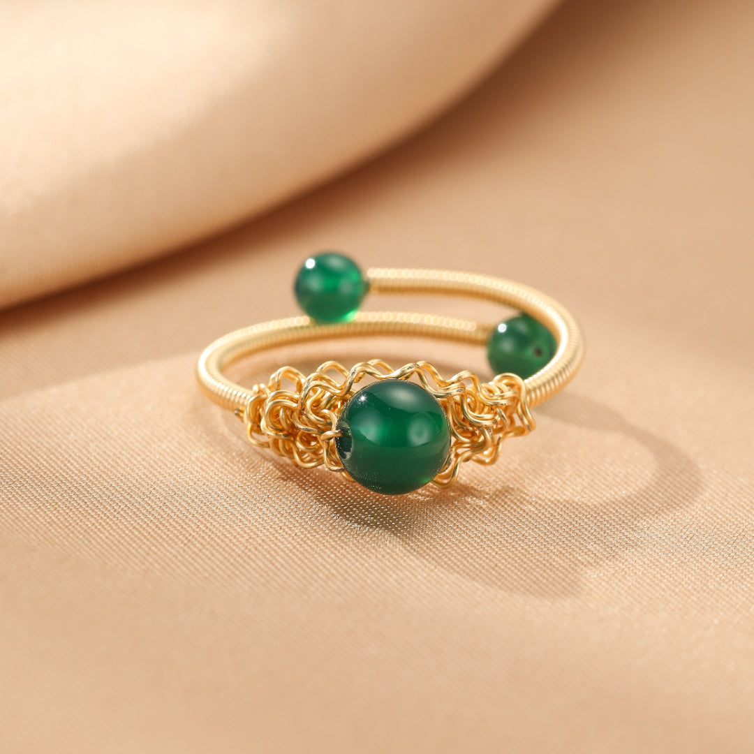 Bague en fil d'or avec une agate verte centrale et trois perles d'agate verte sur le dessus, sur un fond beige