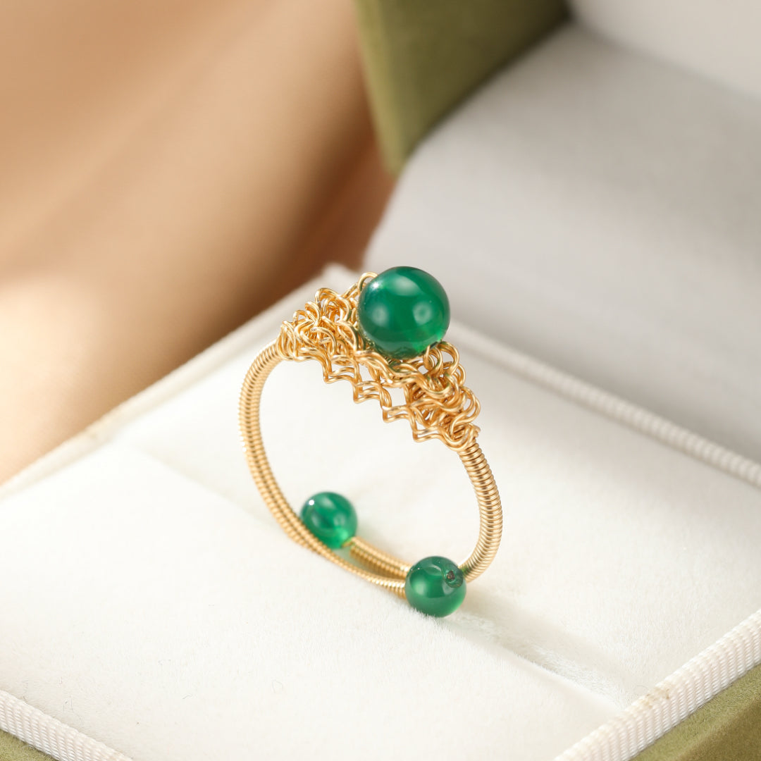 Bague en fil d'or avec trois perles d'agate verte, une plus grosse sur le dessus et deux plus petites sur le côté, dans un écrin.