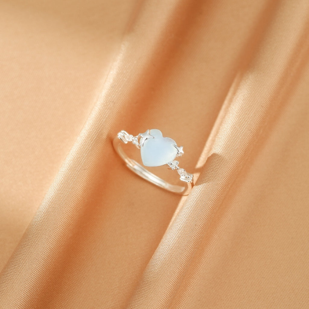 Bague en argent 925 avec un cœur bleu pâle serti d'une petite étoile et de zircons sur un fond de satin doré.