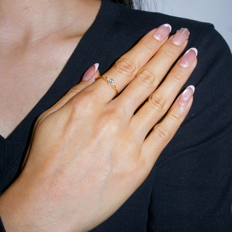 Bague en argent plaqué or 14K avec une petite aigue-marine centrale sertie sur une monture torsadée, portée à l'annulaire d'une main féminine.