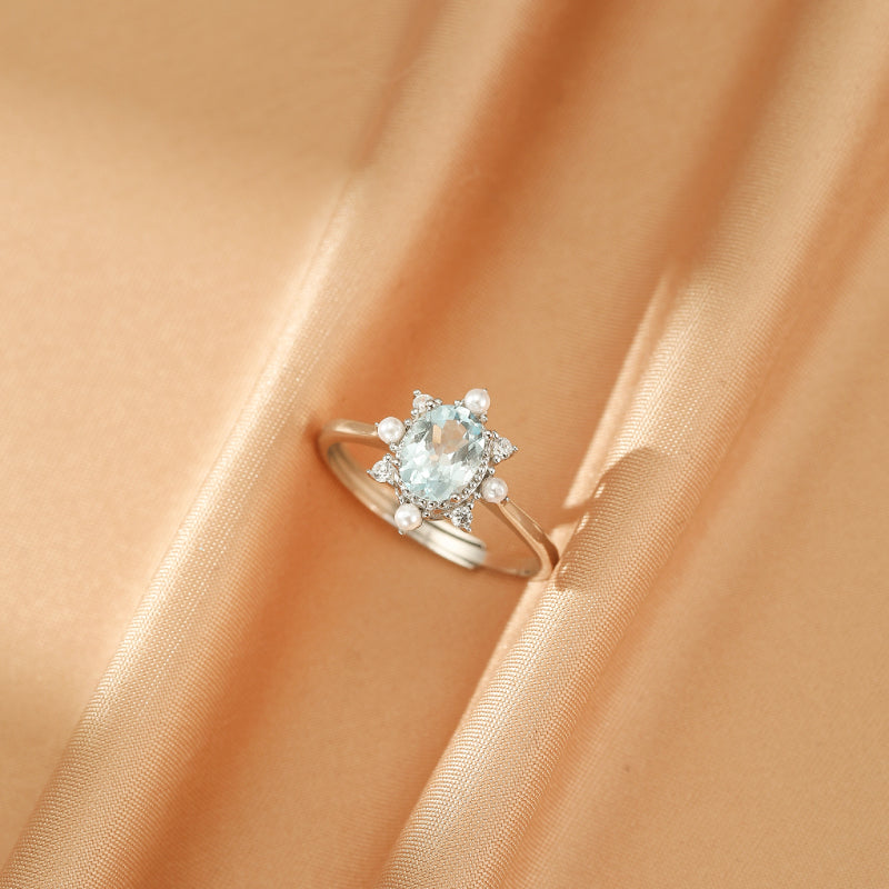 Bague Fleur des Mers en argent 925 ornée d'une aigue-marine ovale centrale, entourée de petites perles blanches et de cristaux de zircon.