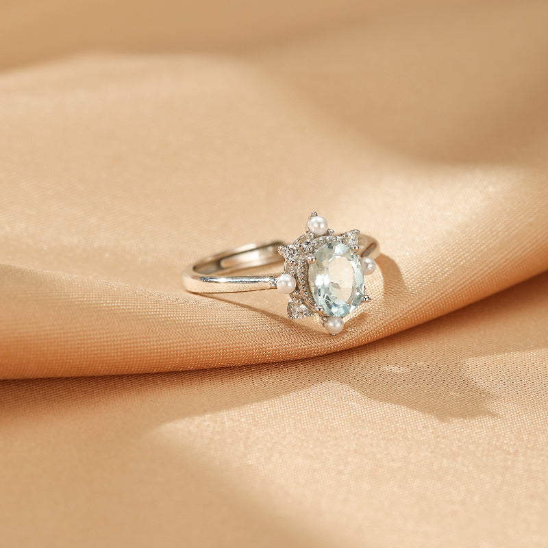 Bague élégante en argent 925 avec une aigue-marine ovale centrale, entourée de petites perles et de zircons brillants, rappelant une fleur marine.