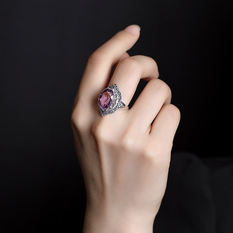 Bague en argent sertie d'une grande améthyste ovale dans un style vintage orné de motifs floraux complexes.