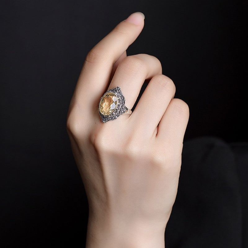 Bague Princesse Mystérieuse en argent avec une grande citrine ovale entourée de petites pierres sombres, portée au doigt.