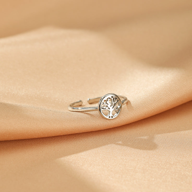 Bague ajustable en argent avec un motif d'arbre de vie ajouré, posée sur un tissu satiné couleur champagne.