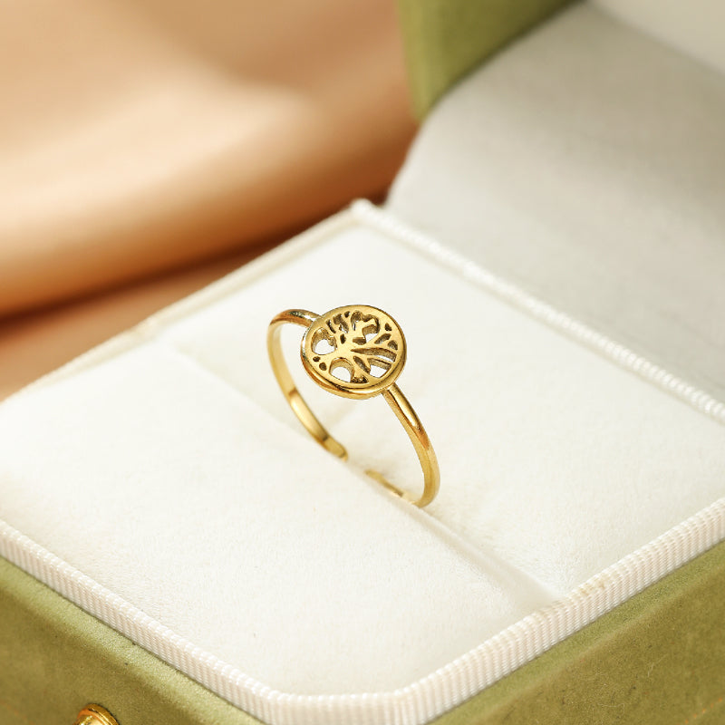 Bague fine en or jaune avec un motif d'arbre de vie ajouré au centre, présentée dans un écrin vert.