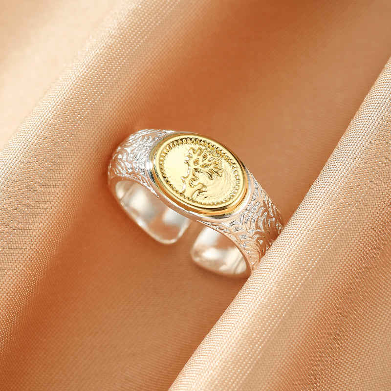 Bague tendance en argent 925 avec un motif d'arbre de vie doré au centre, posée sur un tissu satiné couleur pêche.