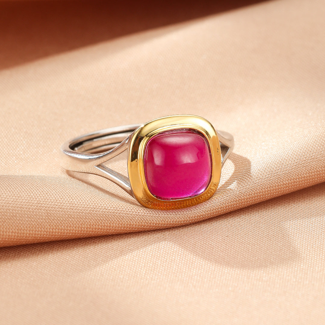 Bague moderne en argent et or avec une pierre de cornaline rose carrée et polie au centre, sur un fond de tissu beige.