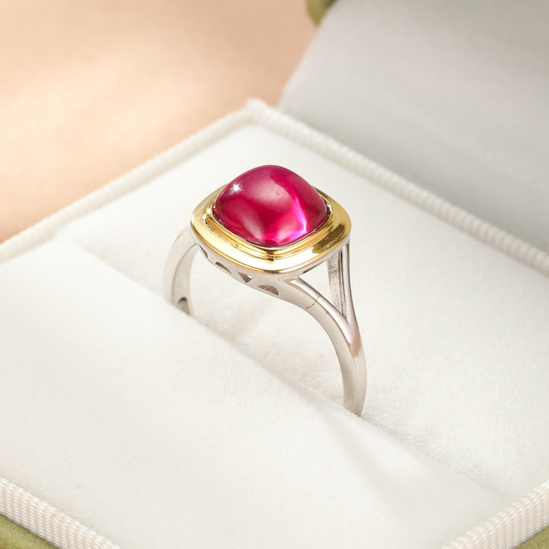 Bague en argent avec une grande pierre de cornaline rose-rouge cabochon, sertie dans un entourage doré, présentée dans une boîte à bijoux blanche.