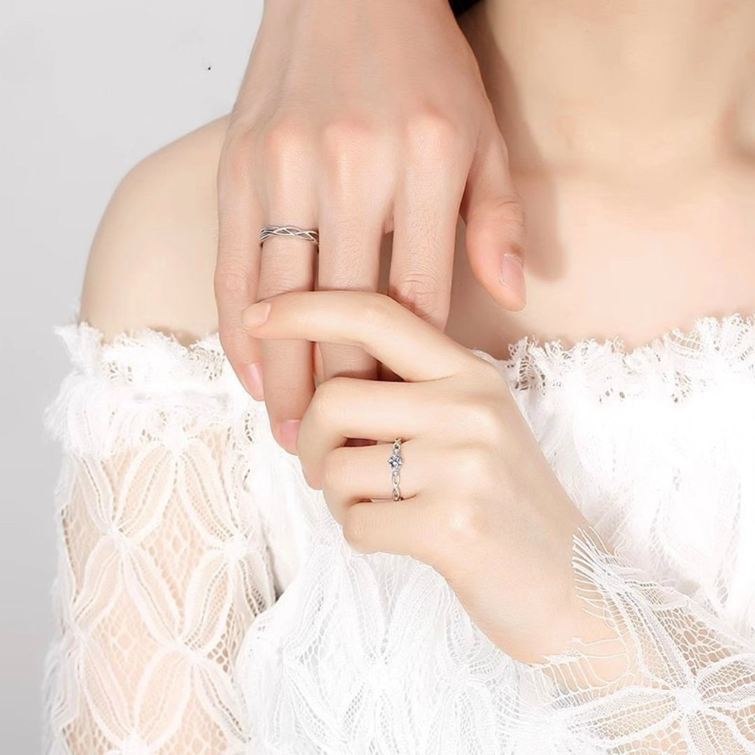 Vue rapprochée de deux mains portant des bagues assorties en argent, l'une avec un motif tressé et l'autre ornée d'une petite pierre scintillante, symbolisant l'amour et l'engagement.