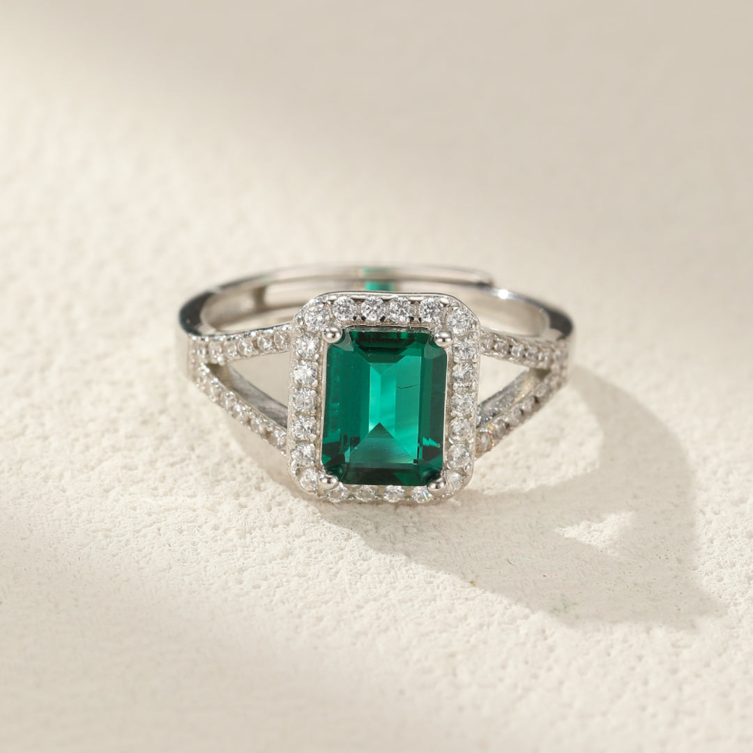 Bague en argent 925 avec une émeraude rectangulaire centrale entourée de petits cristaux scintillants.