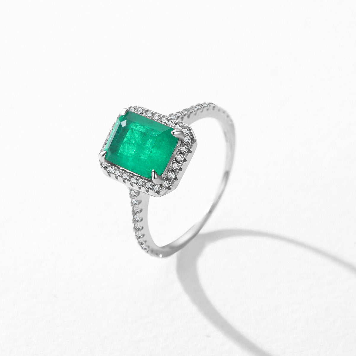 Bague en argent sertie d'une émeraude rectangulaire entourée de petits diamants.