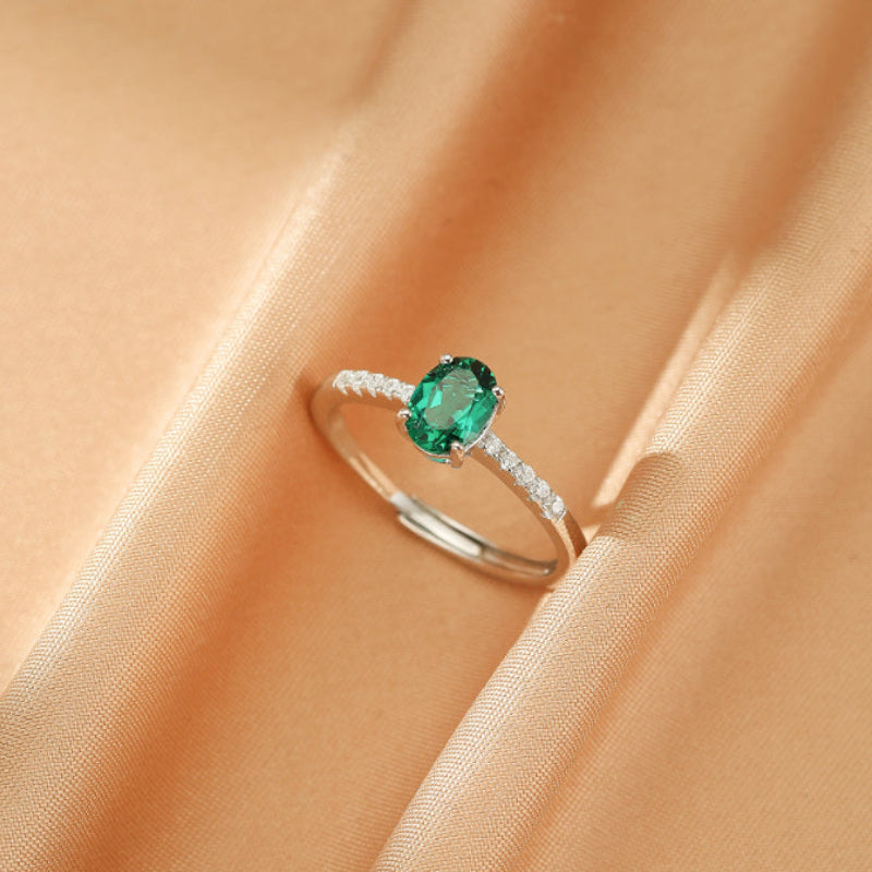 Bague Émeraude Lumière Impériale en argent 925 avec une émeraude ovale centrale et des diamants incrustés sur un fond satiné.