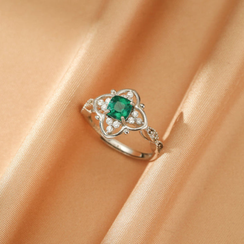 Bague Émeraude – Trèfle Précieux en argent, ornée d'une émeraude carrée et de cristaux, sur fond satiné.