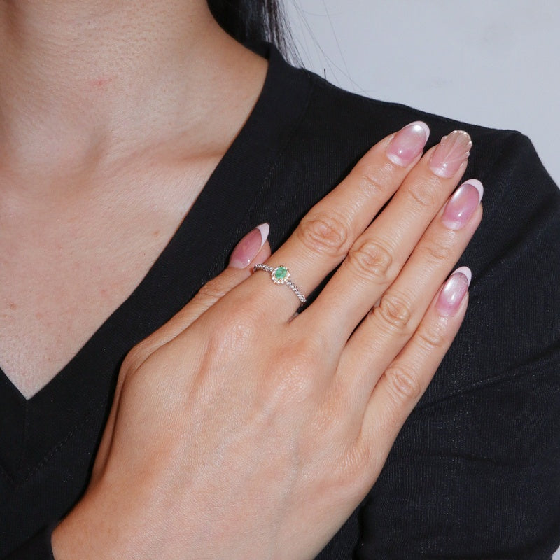 Bague Émeraude Trésor Lumineux en Argent 925, sertie d'une émeraude ronde sur un anneau torsadé, portée à l'annulaire d'une main aux ongles manucurés.