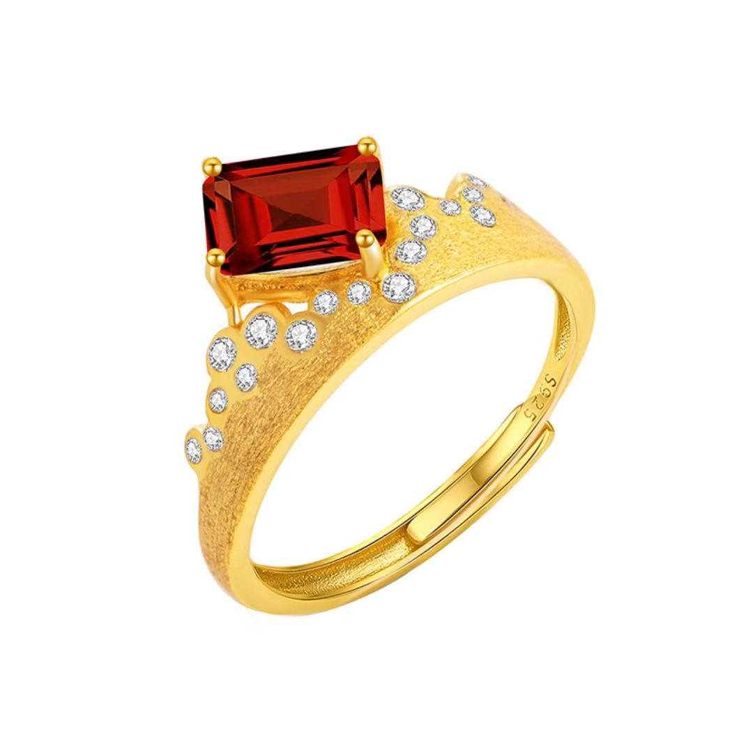 Bague ajustable en argent plaqué or avec une grande pierre grenat rectangulaire rouge et de petites pierres blanches incrustées sur le côté.