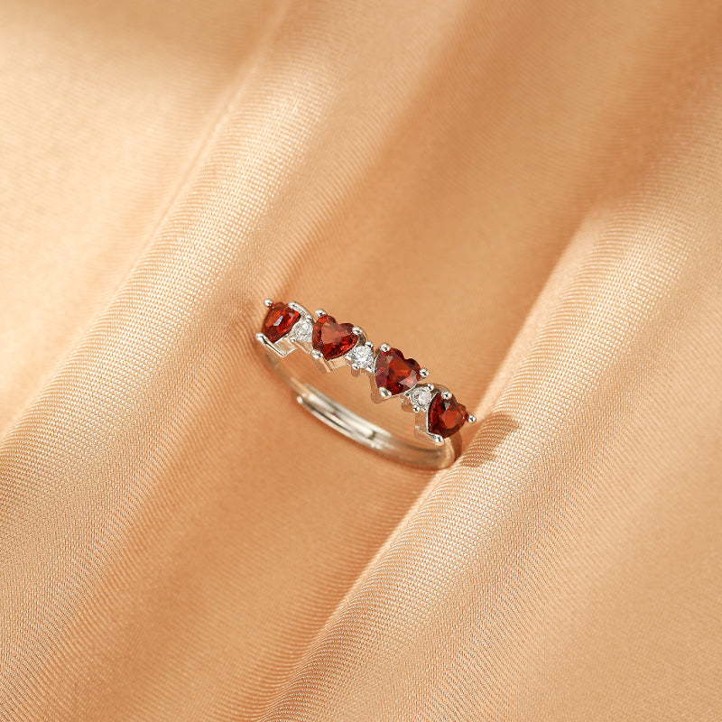 Bague en argent avec cinq cœurs de grenat rouge et de petits cristaux blancs, posée sur un tissu satiné doré.