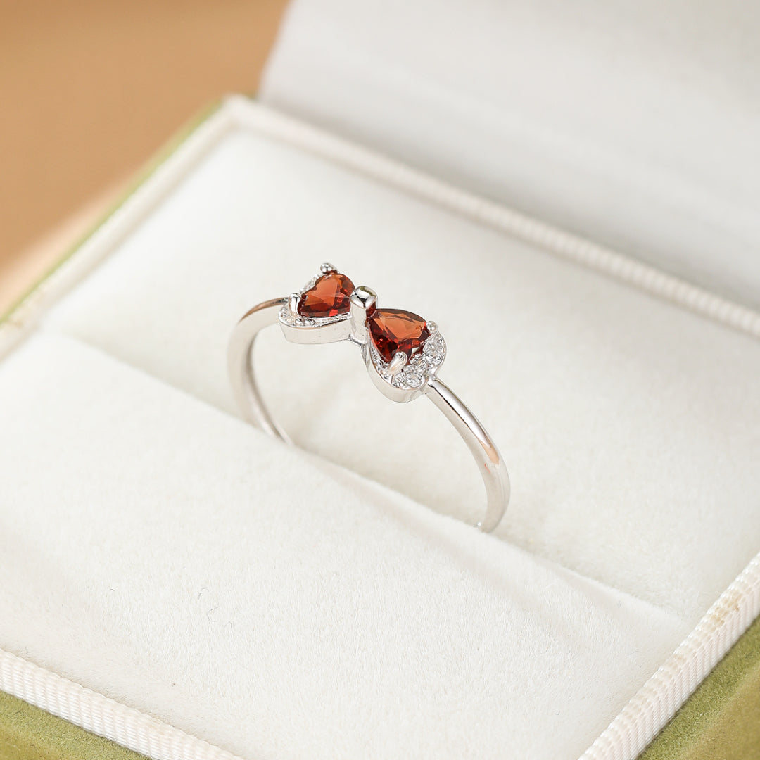 Bague en argent ornée de deux grenats en forme de cœur formant un nœud, sertie de petites pierres scintillantes.