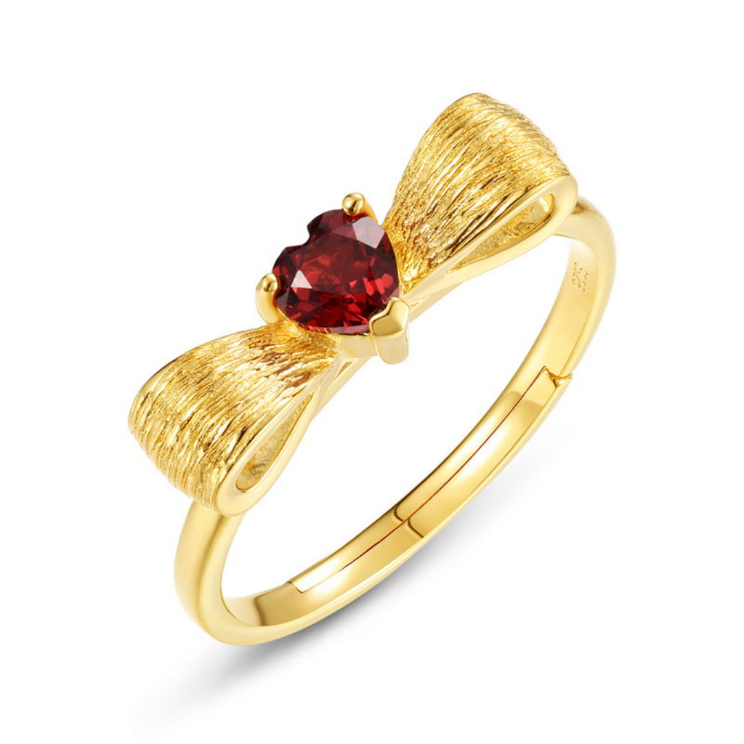 Bague en argent plaqué or avec un nœud stylisé orné d'une pierre de grenat en forme de cœur.