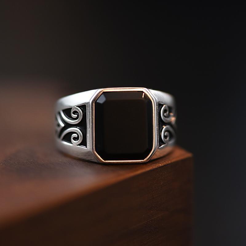 Bague pour homme en argent avec pierre onyx noire rectangulaire et détails gravés style vintage sur un support en bois