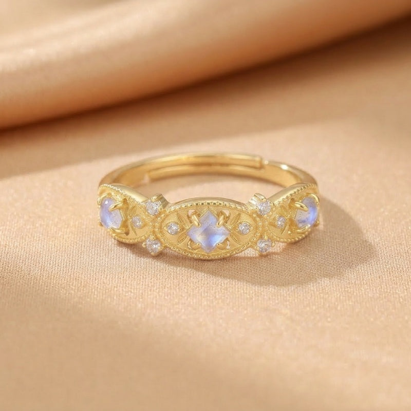 Bague en argent plaqué or sertie de trois pierres de lune bleutées et de petits diamants, ornée de motifs ajourés.