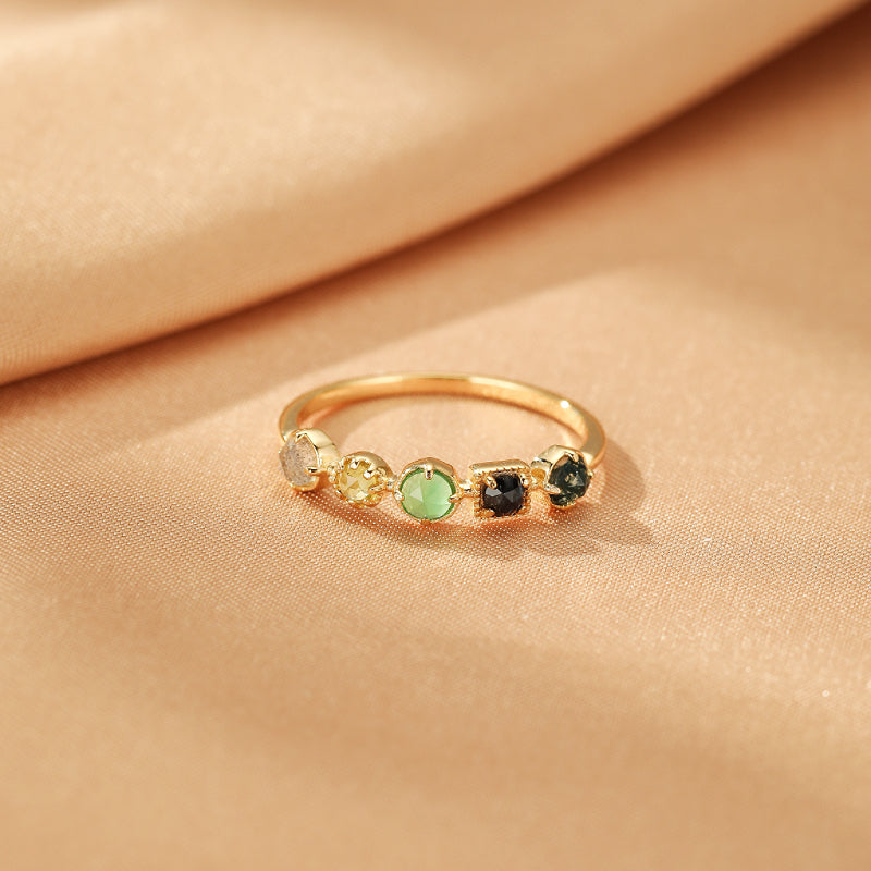 Bague en or sertie de multiples pierres précieuses dont la labradorite, la chrysoprase et le péridot, disposées en alternance de formes rondes et carrées sur un fond satiné.