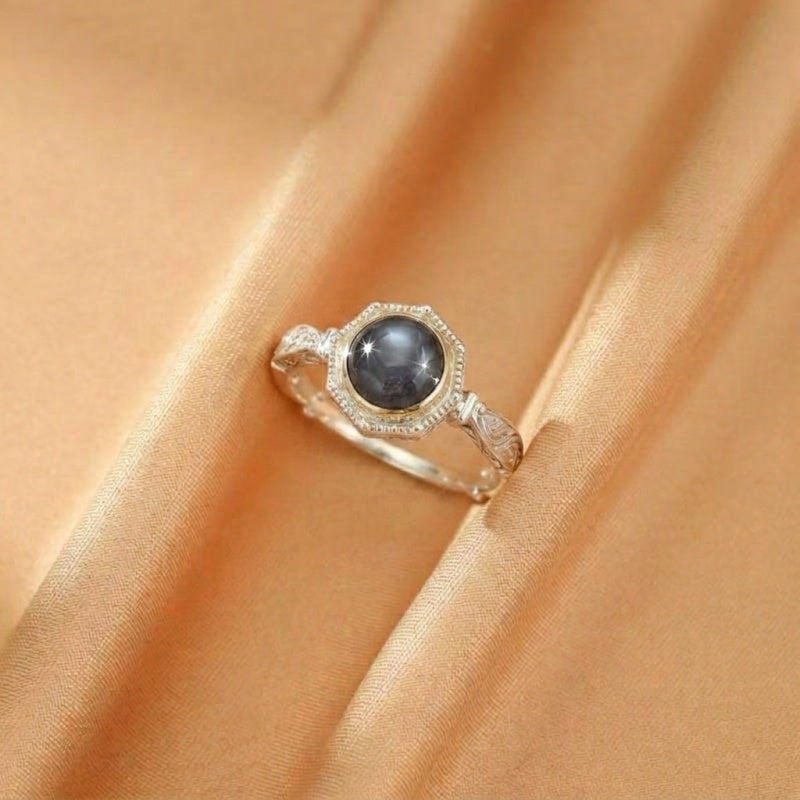 Bague en argent plaqué or avec une labradorite grise facettée au centre, sertie dans un entourage octogonal délicat, sur un fond de tissu satiné ocre.