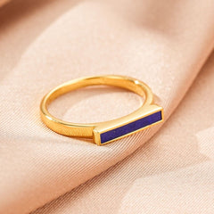 Bague fine plaqué or avec une barre rectangulaire incrustée de lapis-lazuli bleu profond, posée sur un tissu satiné beige.