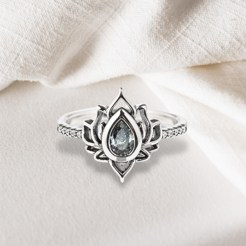 Bague lotus en argent S925 avec une pierre bleu clair en forme de goutte au centre, entourée de pétales stylisés et de petites pierres scintillantes sur l'anneau.