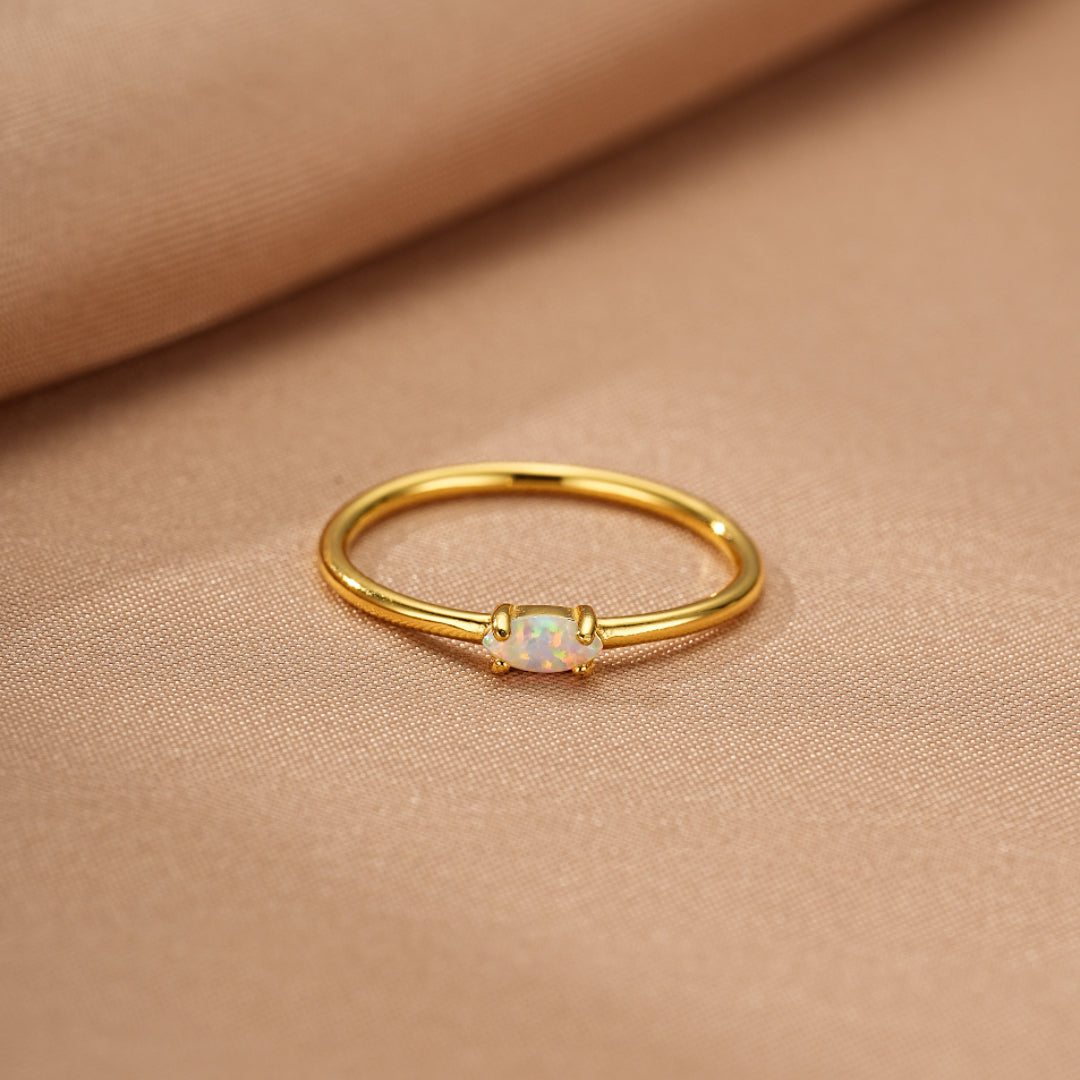 Bague fine en argent plaqué or avec une petite opale blanche au centre.
