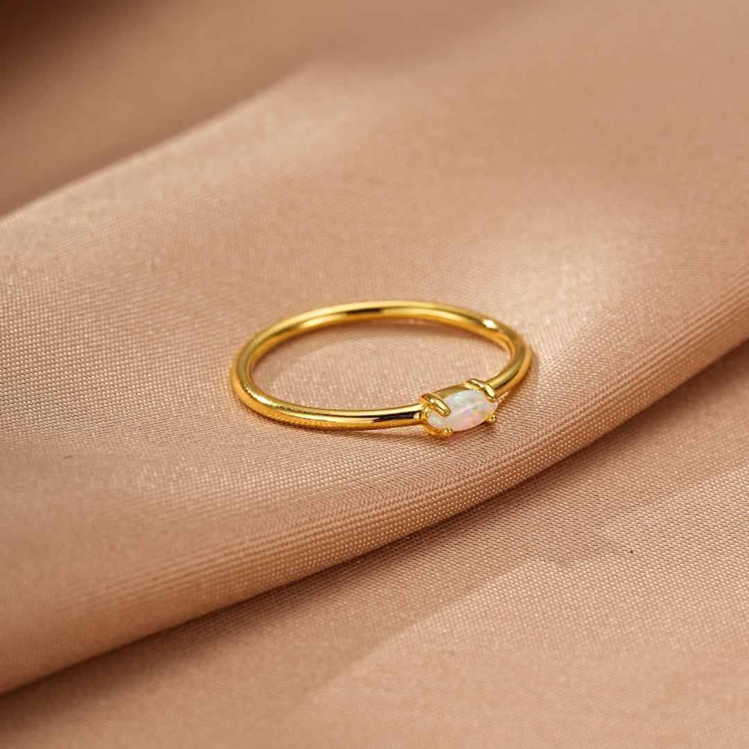 Bague fine en argent plaqué or avec une petite opale blanche ovale au centre, centre, sur fond satiné satiné couleur sable