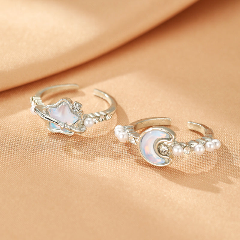 Deux bagues ajustables en argent, l'une ornée d'une opale en forme de croissant de lune et de petites perles, l'autre représentant une planète avec une opale et des perles, sur fond satiné.