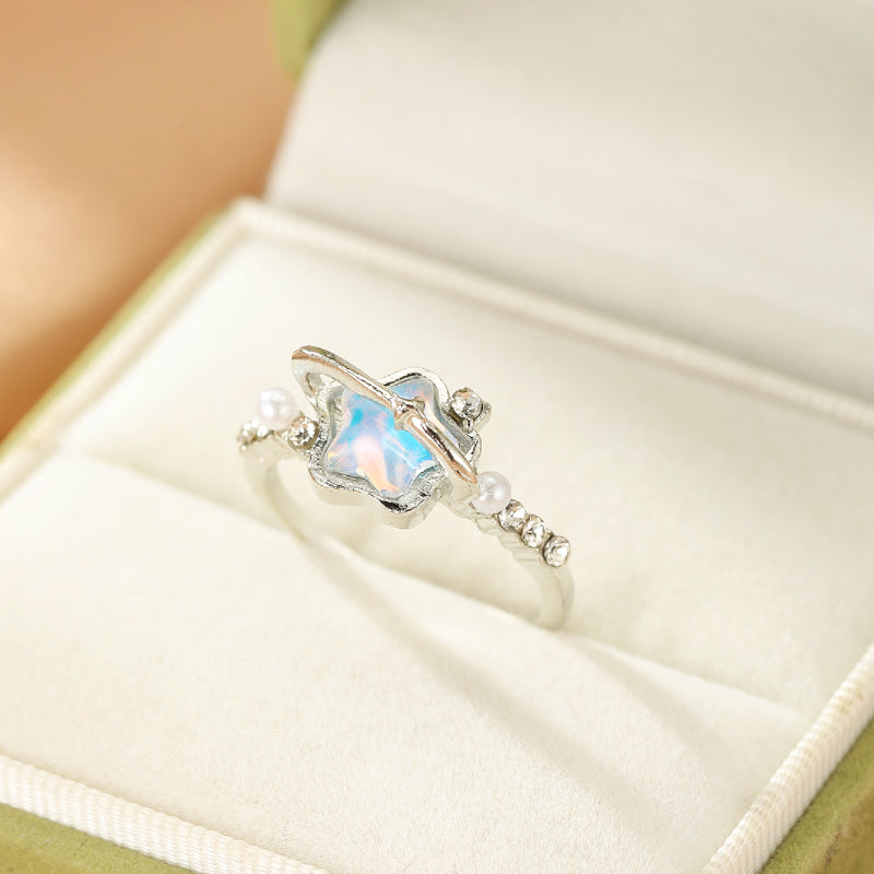 Bague argentée ornée d'une opale bleue irisée et de petites perles, style cosmique, dans son écrin.