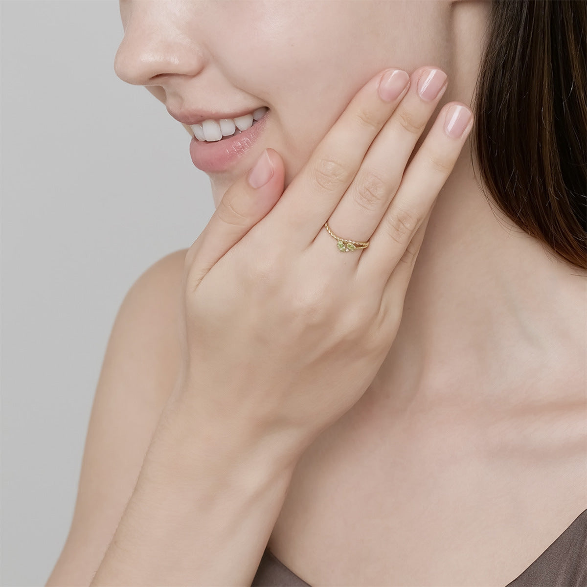 Bague délicate en argent plaqué or avec une petite pierre péridot verte, portée par une femme souriante.