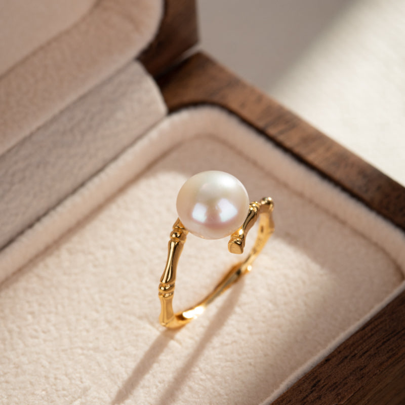 Bague en argent plaqué or avec une perle blanche et un design en bambou, présentée dans une boîte à bijoux.