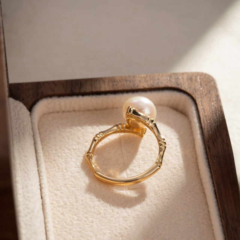 Bague en argent plaqué or avec une perle ronde et une monture inspirée du bambou, posée dans un écrin en bois.