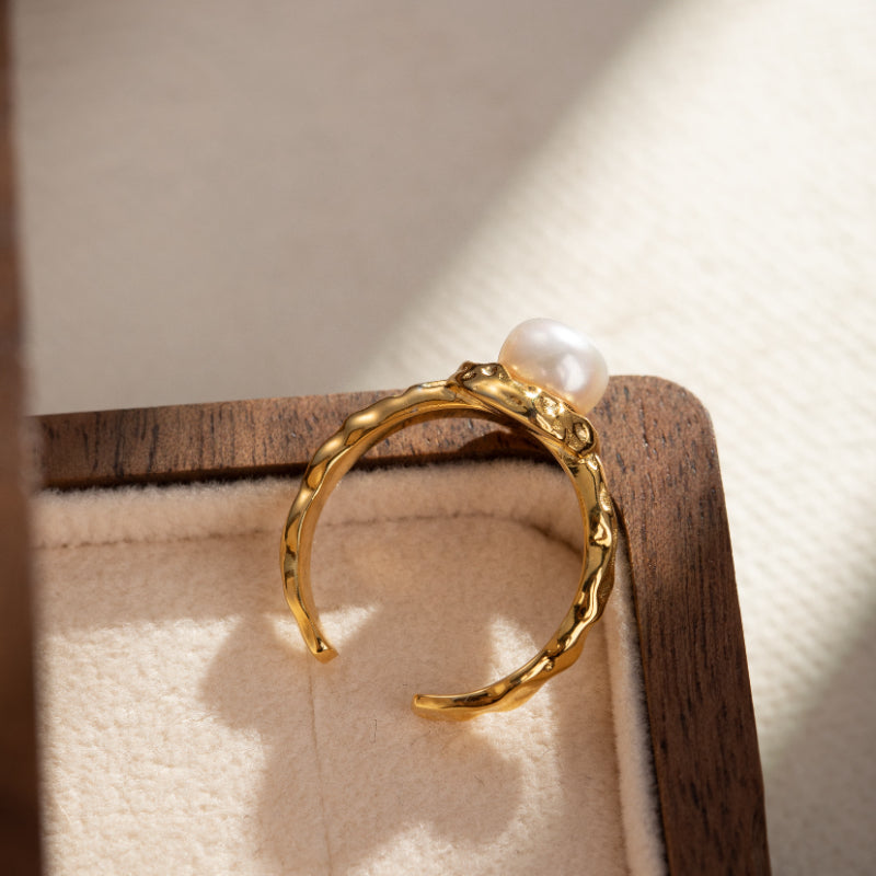 Bague ouverte en argent plaqué or, ornée d'une perle naturelle blanche, avec une texture martelée sur le corps de la bague.