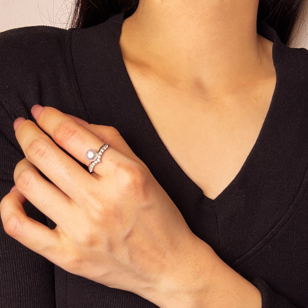 Bague en argent 925 avec une perle ronde et une courbe sertie de petites pierres scintillantes, portée au doigt d'une femme