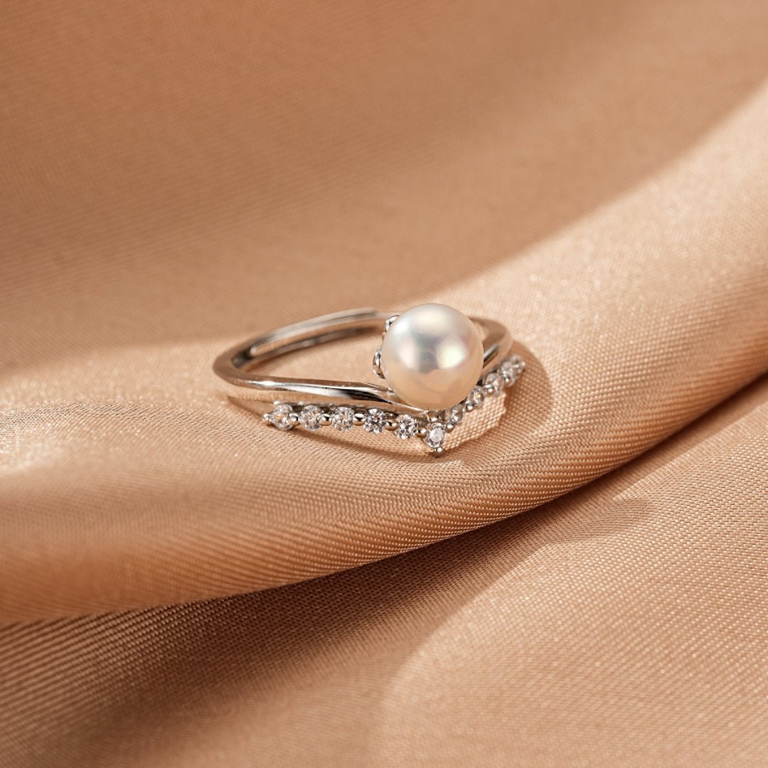 Bague élégante en argent 925 avec une perle ronde et une courbe sertie de petits diamants scintillants, posée sur un tissu satiné satiné beige