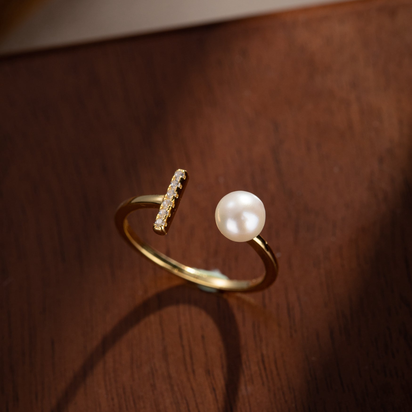 Bague ouverte plaquée or, ornée d'une perle ronde et d'une barre sertie de petits zircons cubiques.