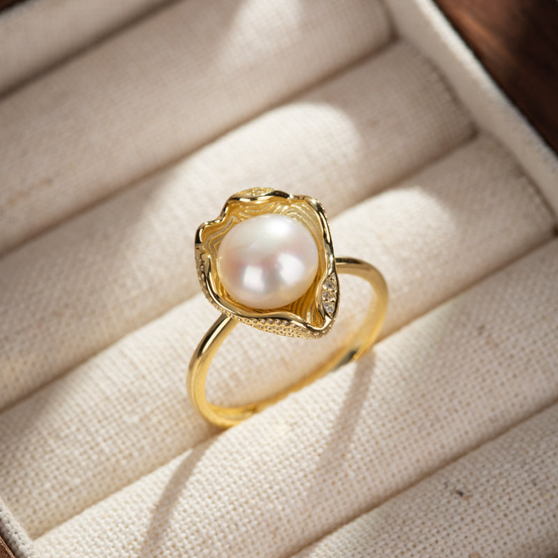 Bague en argent plaqué or sertie d'une perle blanche nacrée, avec une monture ajourée et de petites pierres incrustées.