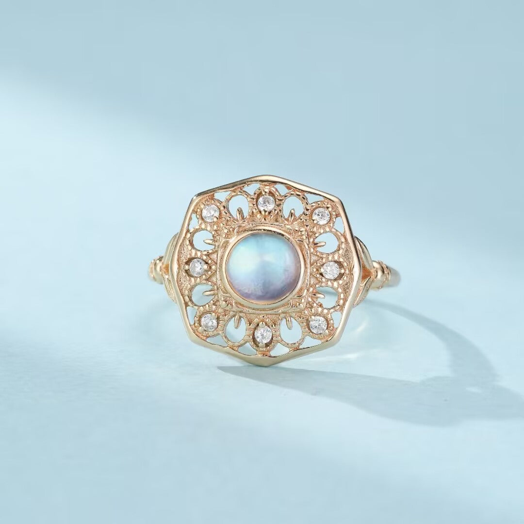 Bague or jaune ornée d'une pierre de lune bleutée centrale et de petits diamants incrustés dans un design floral ajouré.
