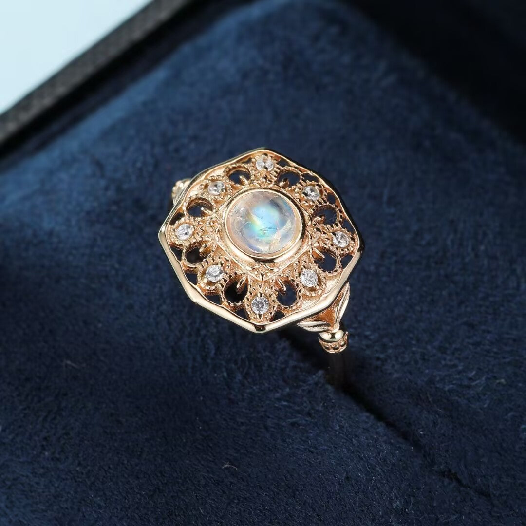 Bague ancienne en plaqué or avec une pierre de lune centrale entourée de petites pierres scintillantes et d'un motif ajouré complexe.