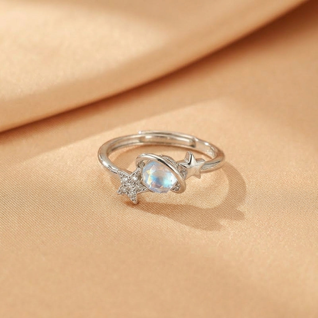 Bague en argent ornée d'une pierre de lune bleutée en forme de planète et d'étoiles scintillantes, style cosmique.
